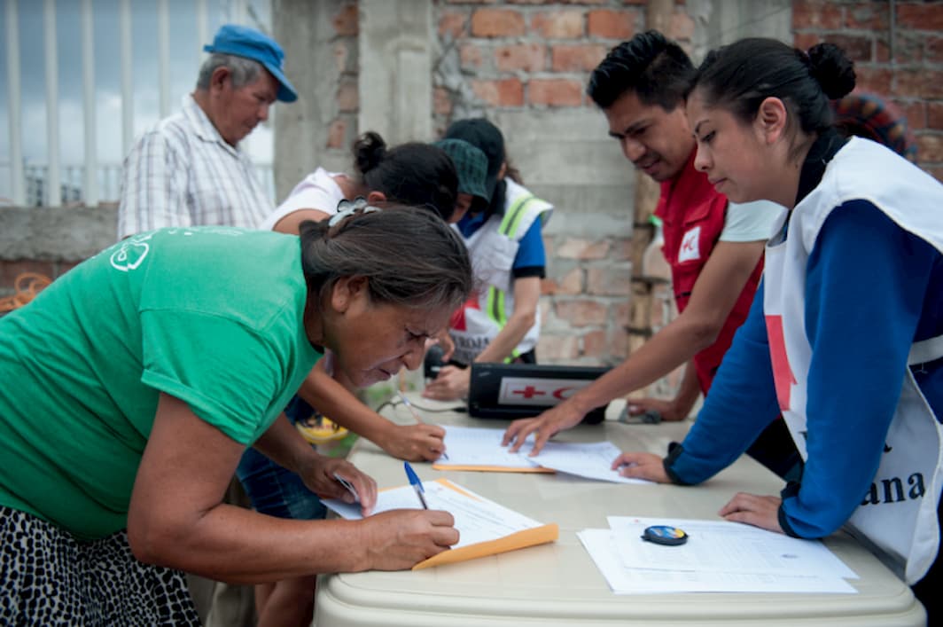 Three Red Cross workers at a temporary station take down information from women at a table outside.